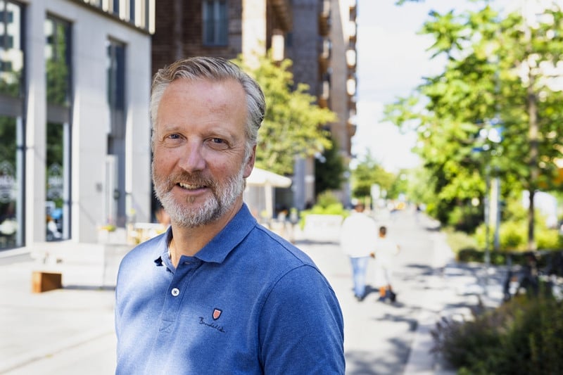 En man i blå skjorta står på en trottoar.