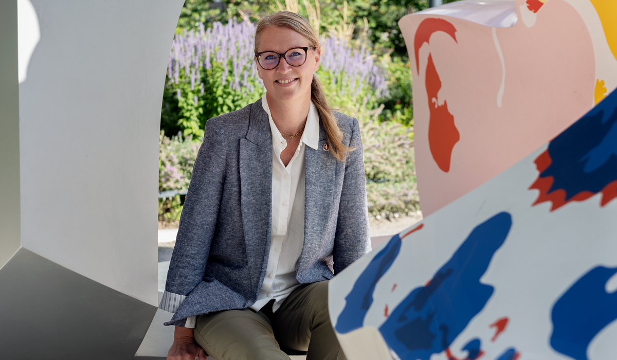 En kvinna sitter p&aring; en b&auml;nk framf&ouml;r en skulptur.