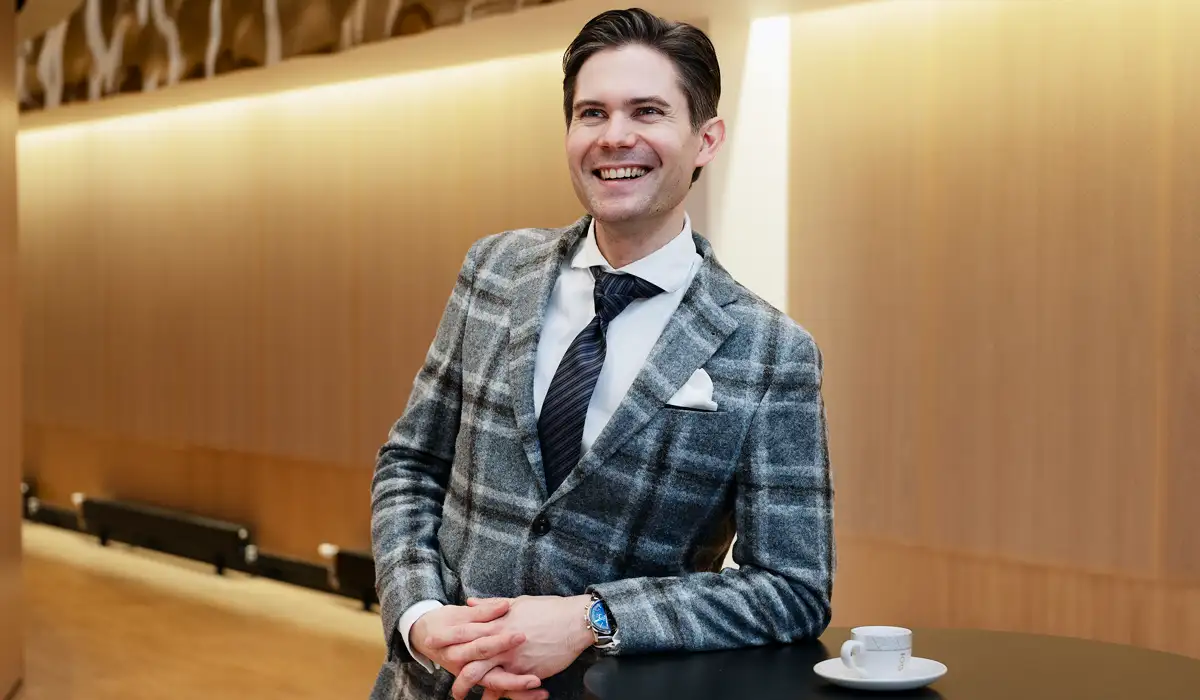 En man i kostym och slips st&aring;r bredvid ett bord.