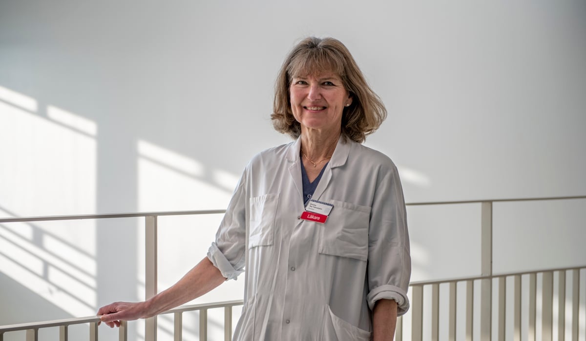 En kvinna i läkarrock står vid ett trappräcke.