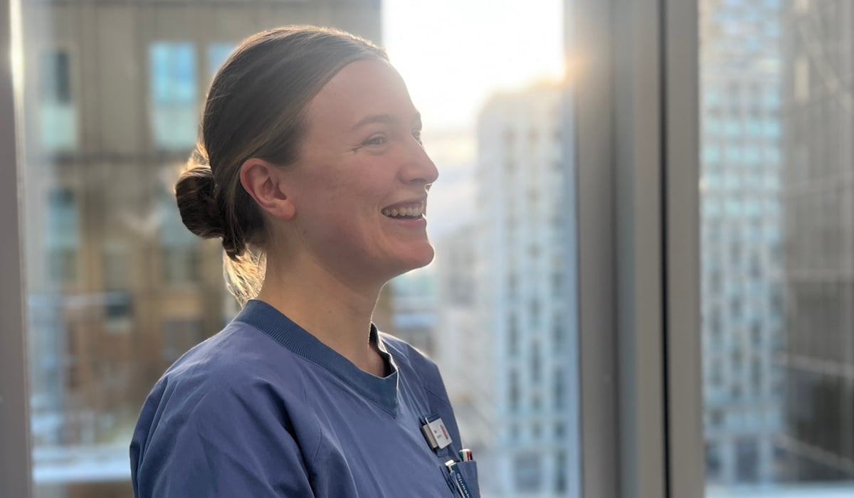 En kvinna i sjukhuskläder står framför ett fönster.