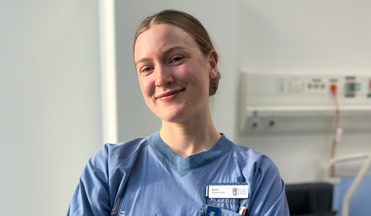 En kvinna i sjukhuskläder står i ett vårdrum.