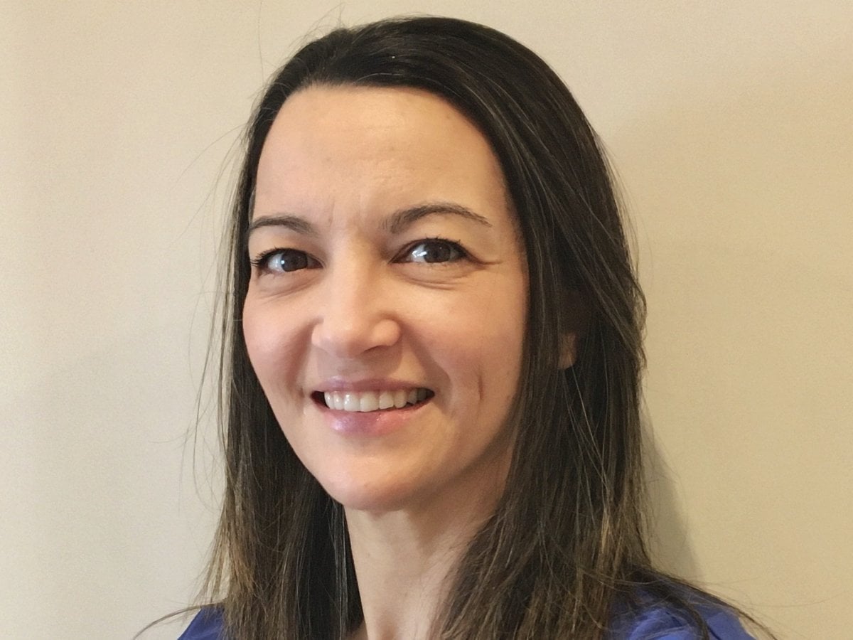 En kvinna med mörkt hål och blå tröja ler.