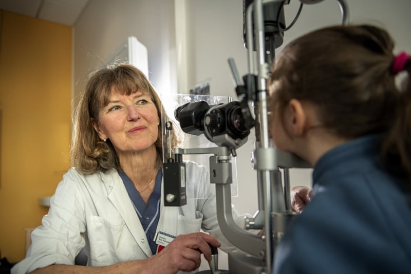 En läkare i vit läkarrock tittar på en patient. Framför sig har hon ett mikroskop.