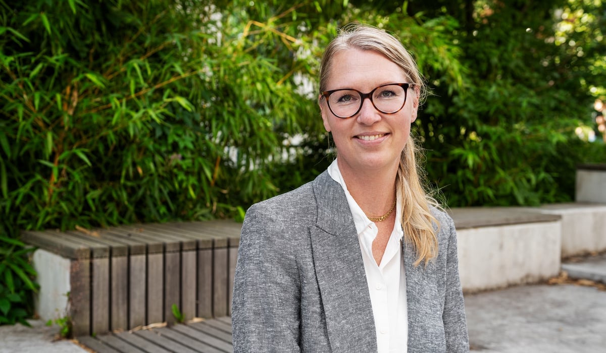 En kvinna med glasögon står framför en träbänk.