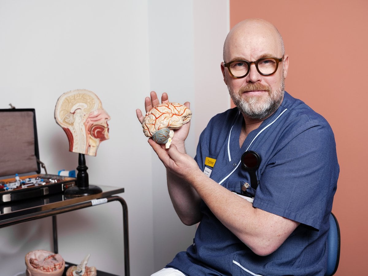 En man i sjukhuskläder håller i en modell av en hjärna.