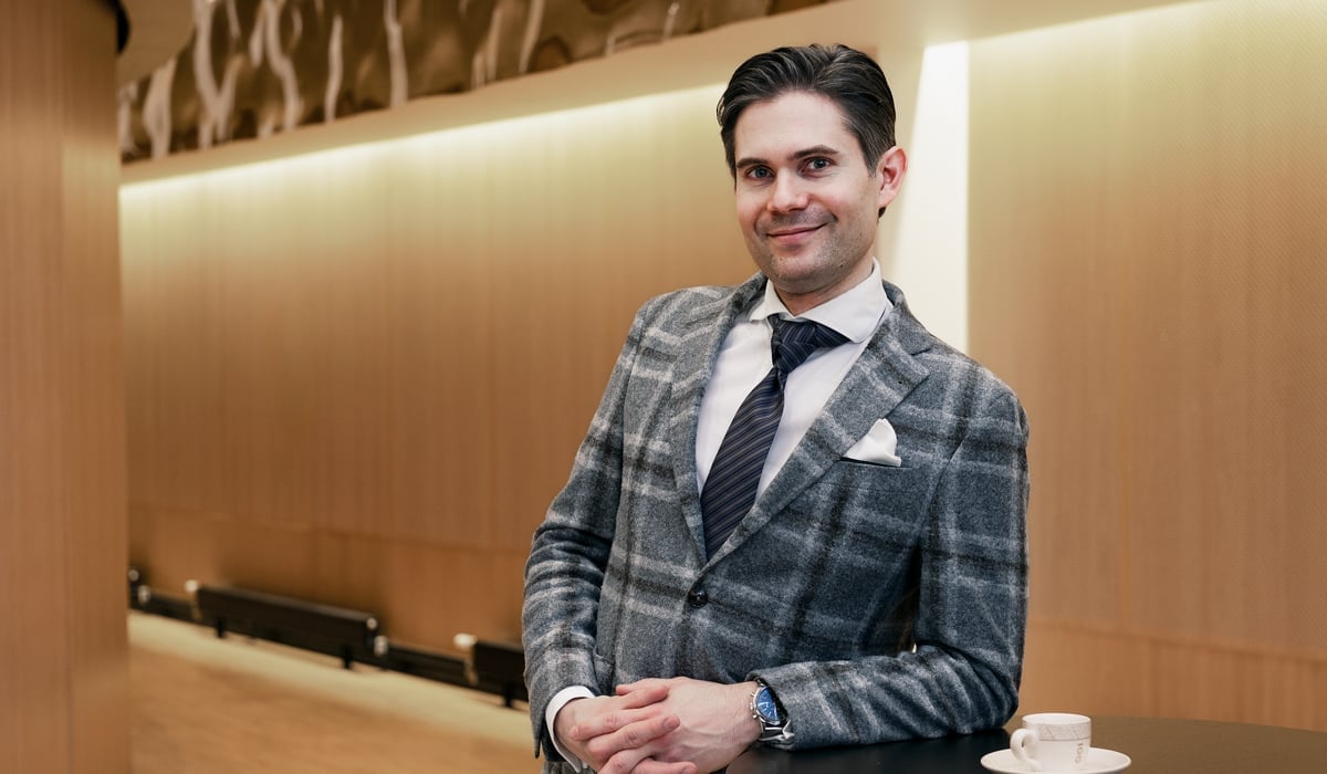 En man i kostym och slips står bredvid ett bord.