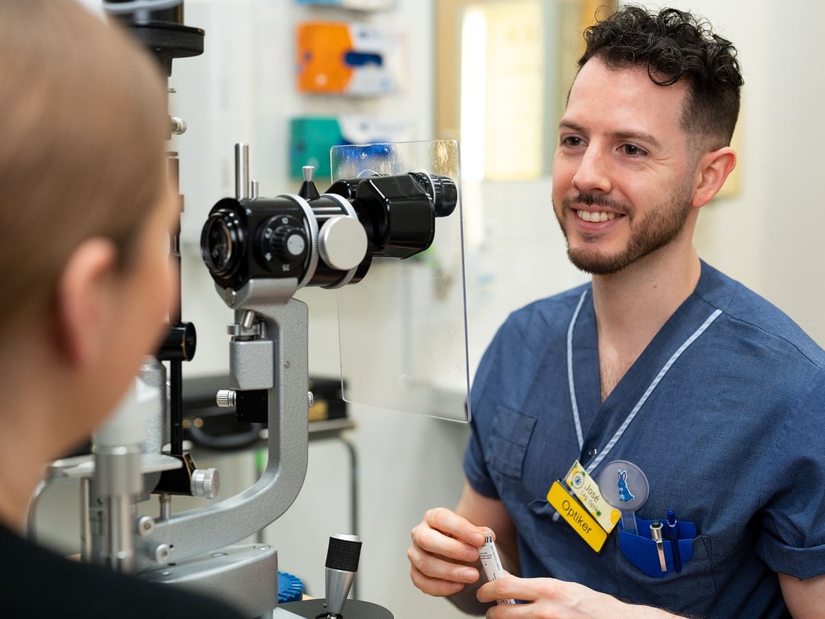 En man i sjukhuskläder sitter bredvid ett mikroskop och tittar mot en patient.