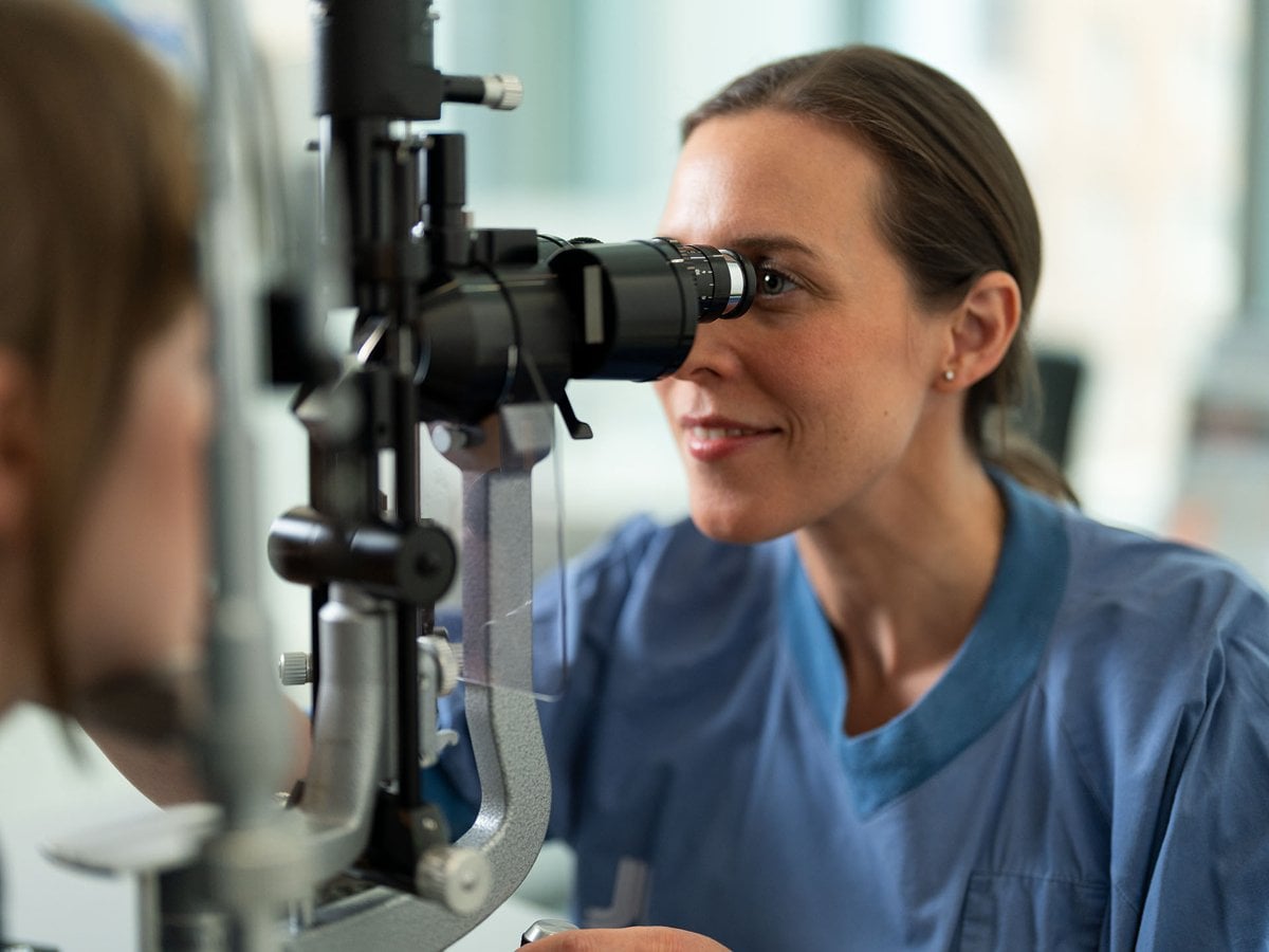 En kvinnlig läkare i blå sjukhuskläder undersöker ögat på en patient.