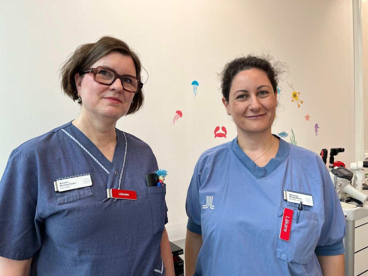 Två personer i sjukhuskläder står bredvid varandra. Den ena har glasögon och mörkt kort hår och den andra har mörkt hår som är uppsatt.