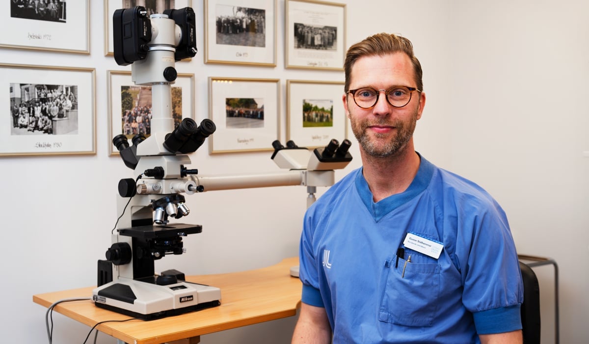 En man i sjukhuskläder bredvid ett mikroskop.