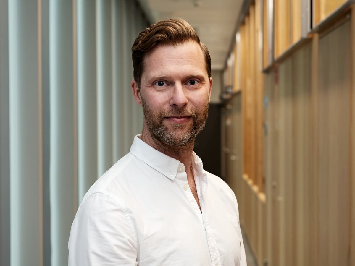 En man i vit skjorta står i en korridor.