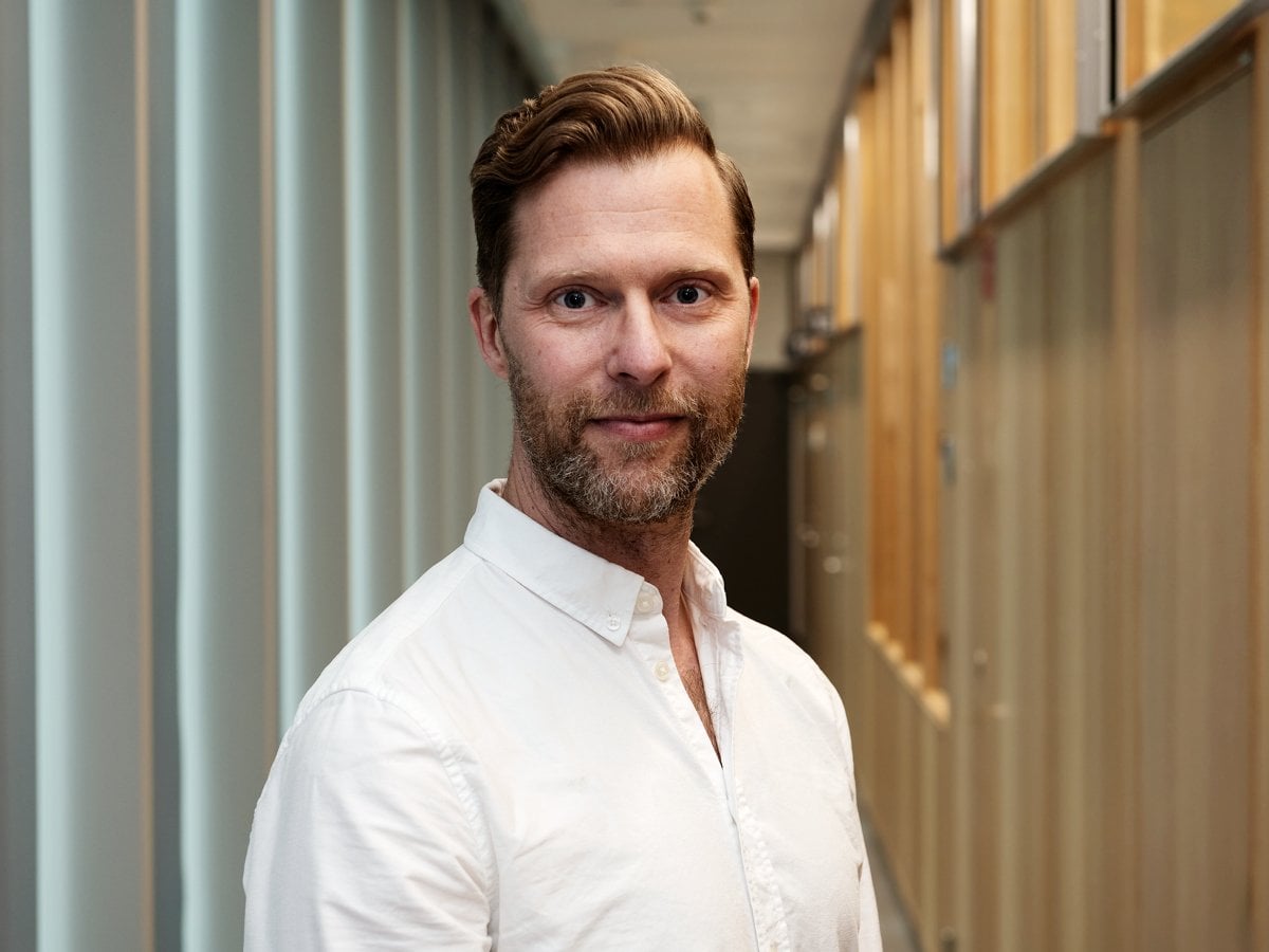 En man i vit skjorta står i en korridor.