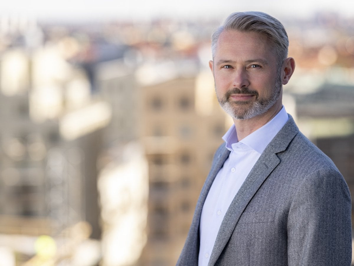 En man i kostym. I bakgrund syns en suddig stadsmiljö.