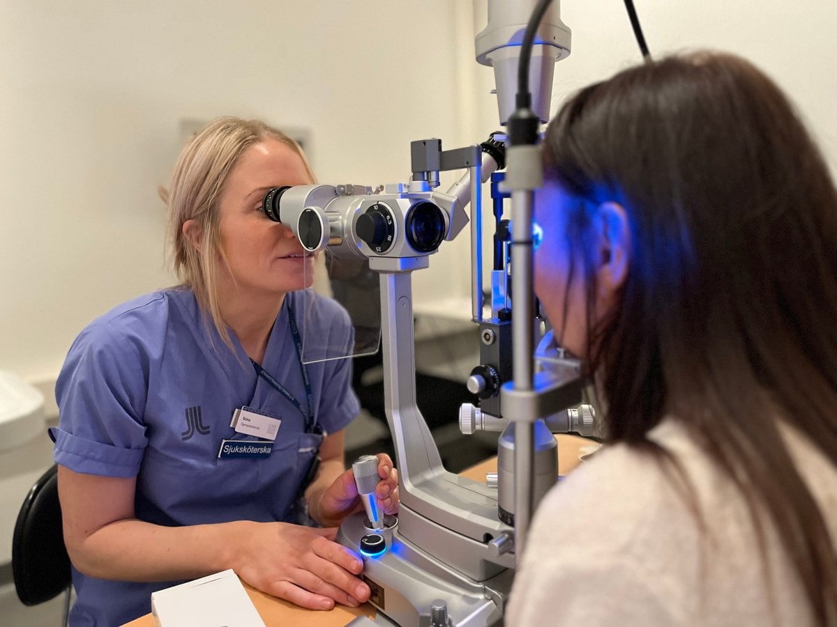 En medarbetare i sjukhuskläder tittar i ett mikroskop.