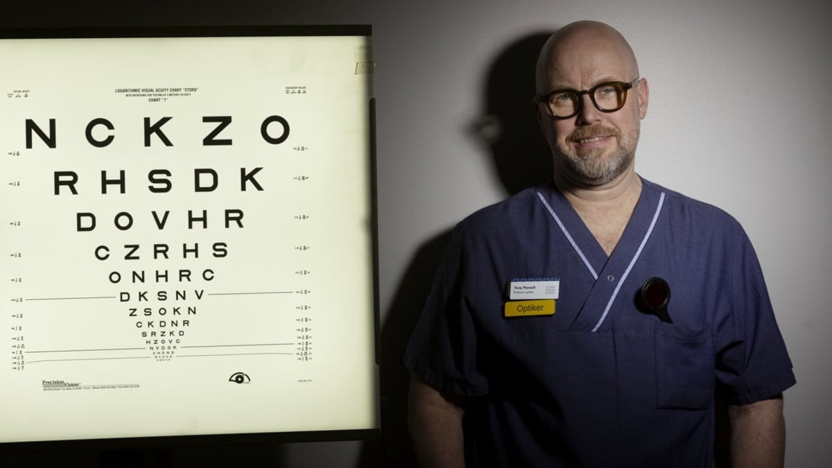 En man i sjukhuskläder står bredvid en syntavla.