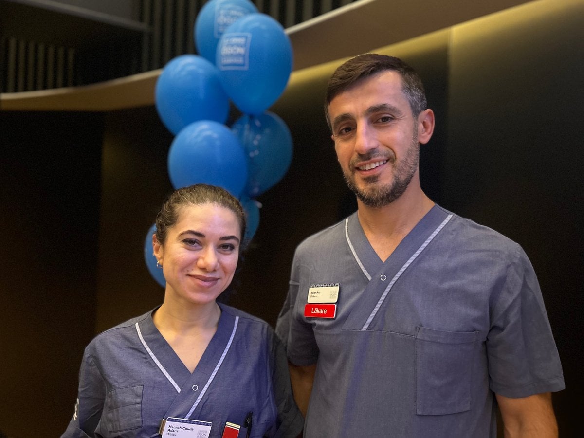 En man och en kvinna som står bredvid varandra. De har vårdkläder och läkarskylt på tröjorna. Ballonger i bakgrunden.