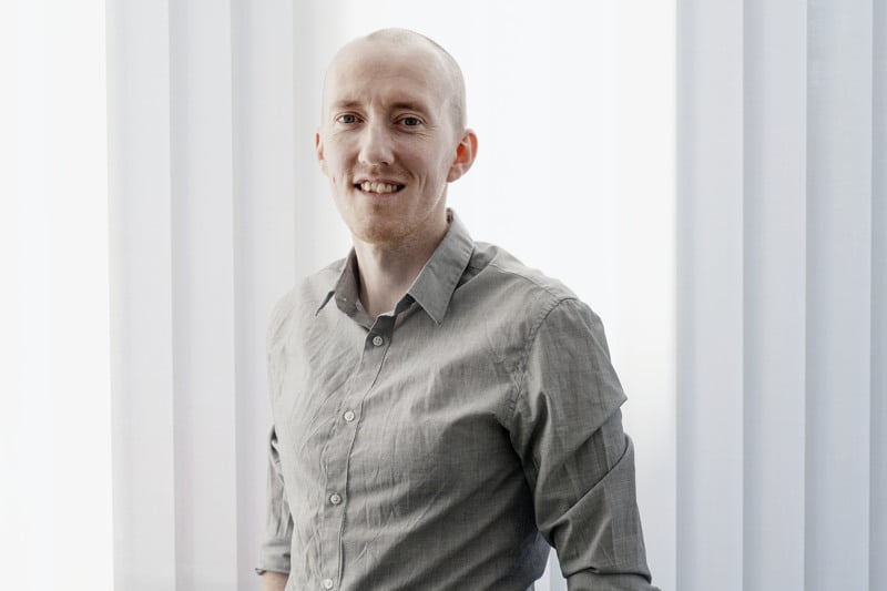 En man som står framför ett fönster med händerna i fickorna.