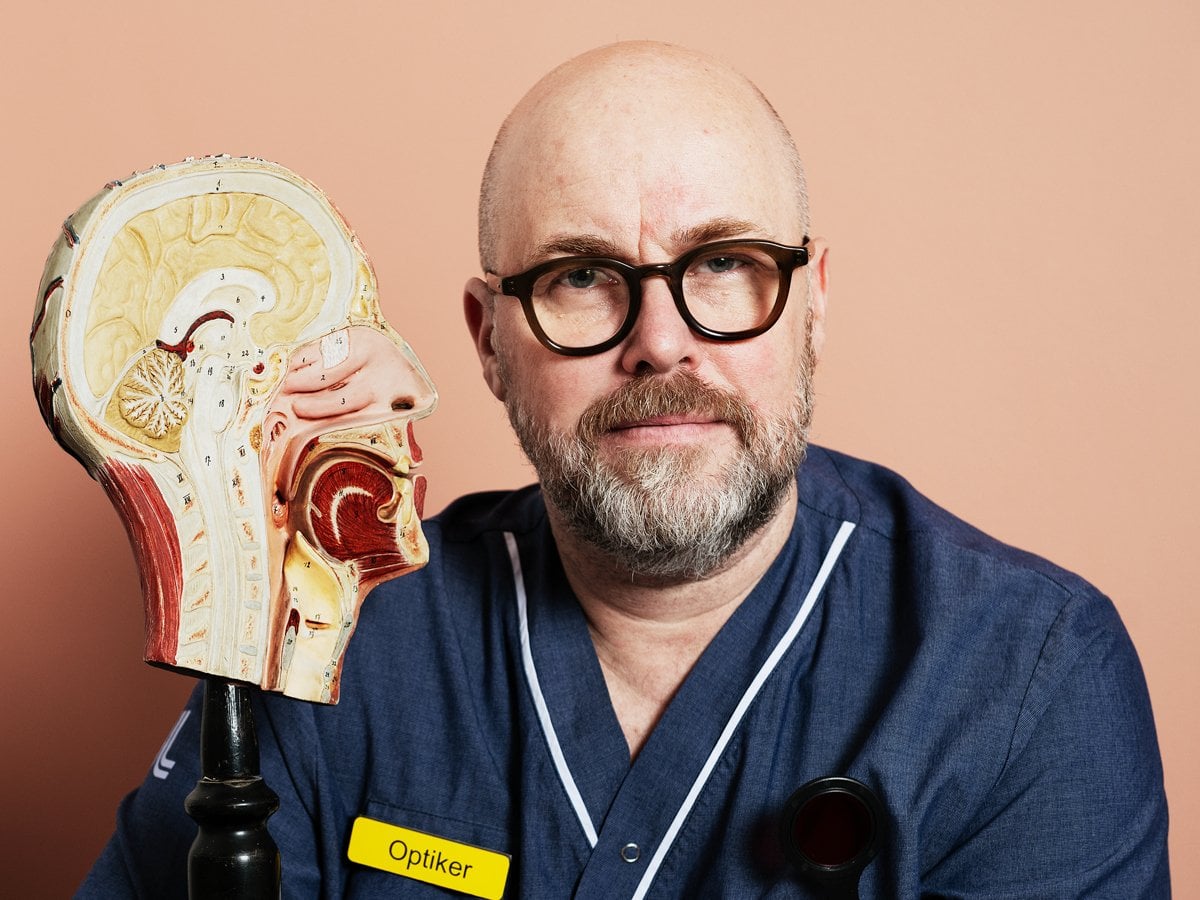 En man med glasögon och sjukhuskläder håller i en modell av ett människohuvud.