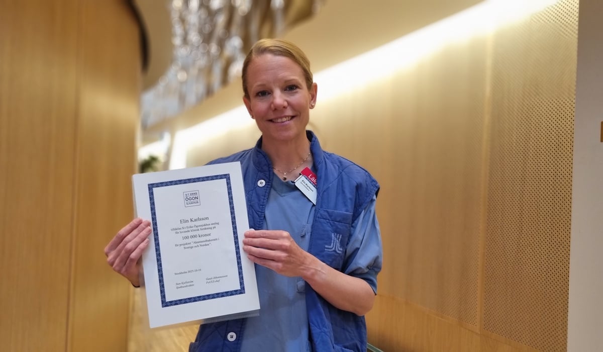 En kvinna i sjukhuskläder håller upp ett certifikat.