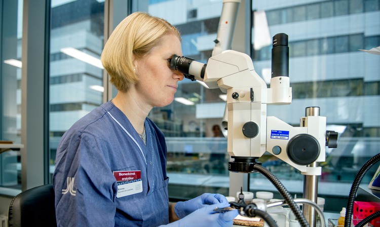 En kvinna i sjukhusuniform som tittar i ett mikroskop.