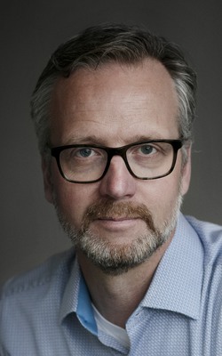 A man with glasses, beard and a blue shirt.